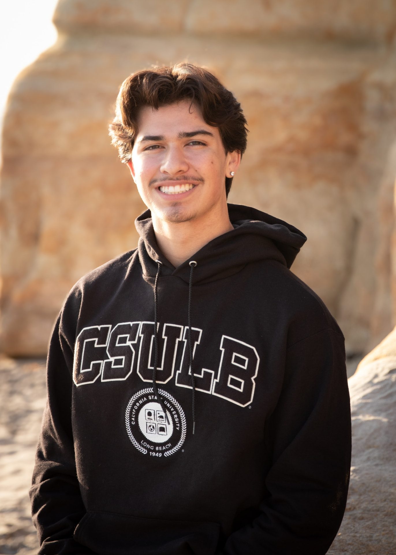 Senior in a CSULB sweatshirt smiling in front of a sandstone bluff
