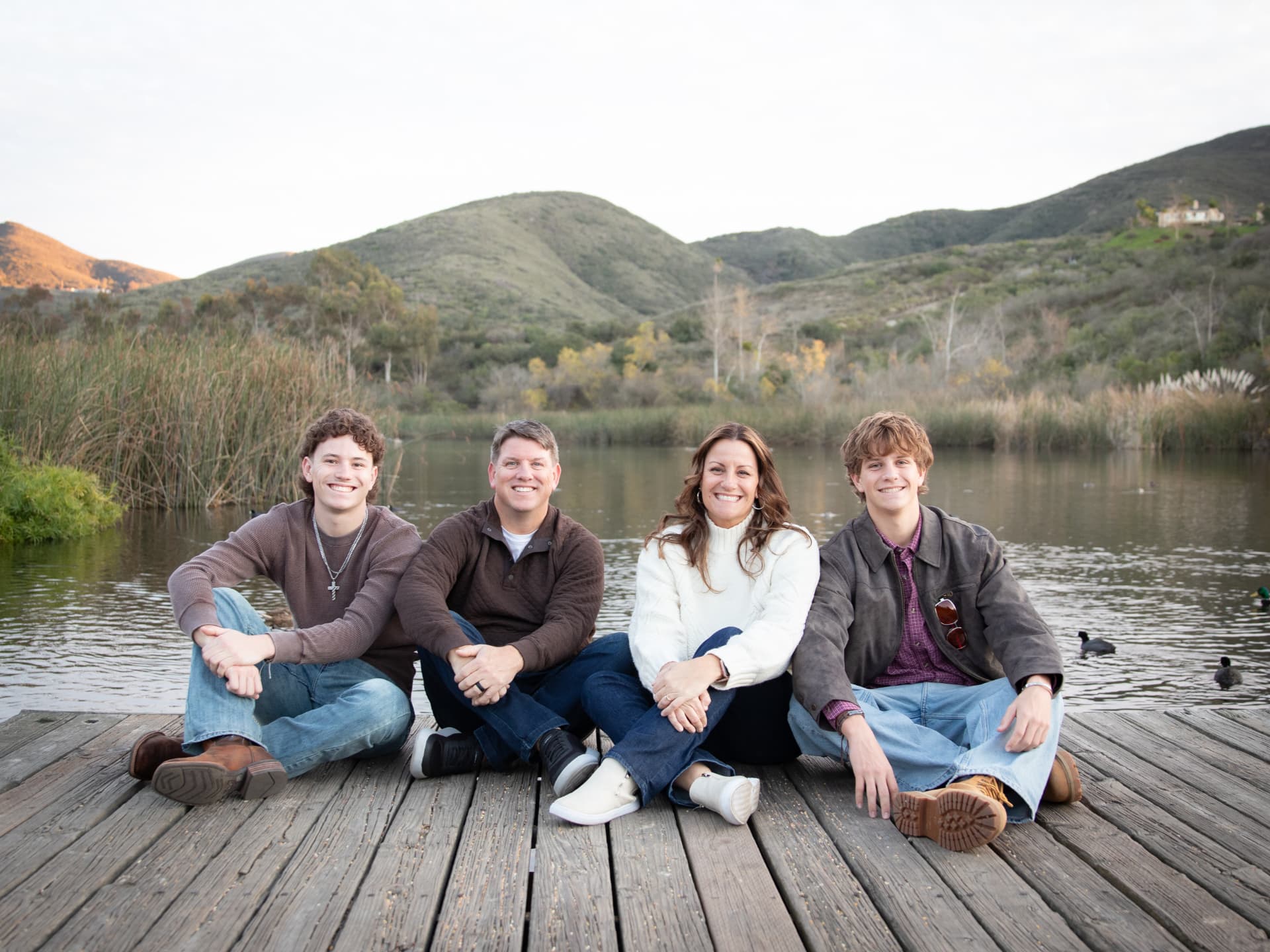 Family of four sitting together on a wooden dock by a lake at sunset