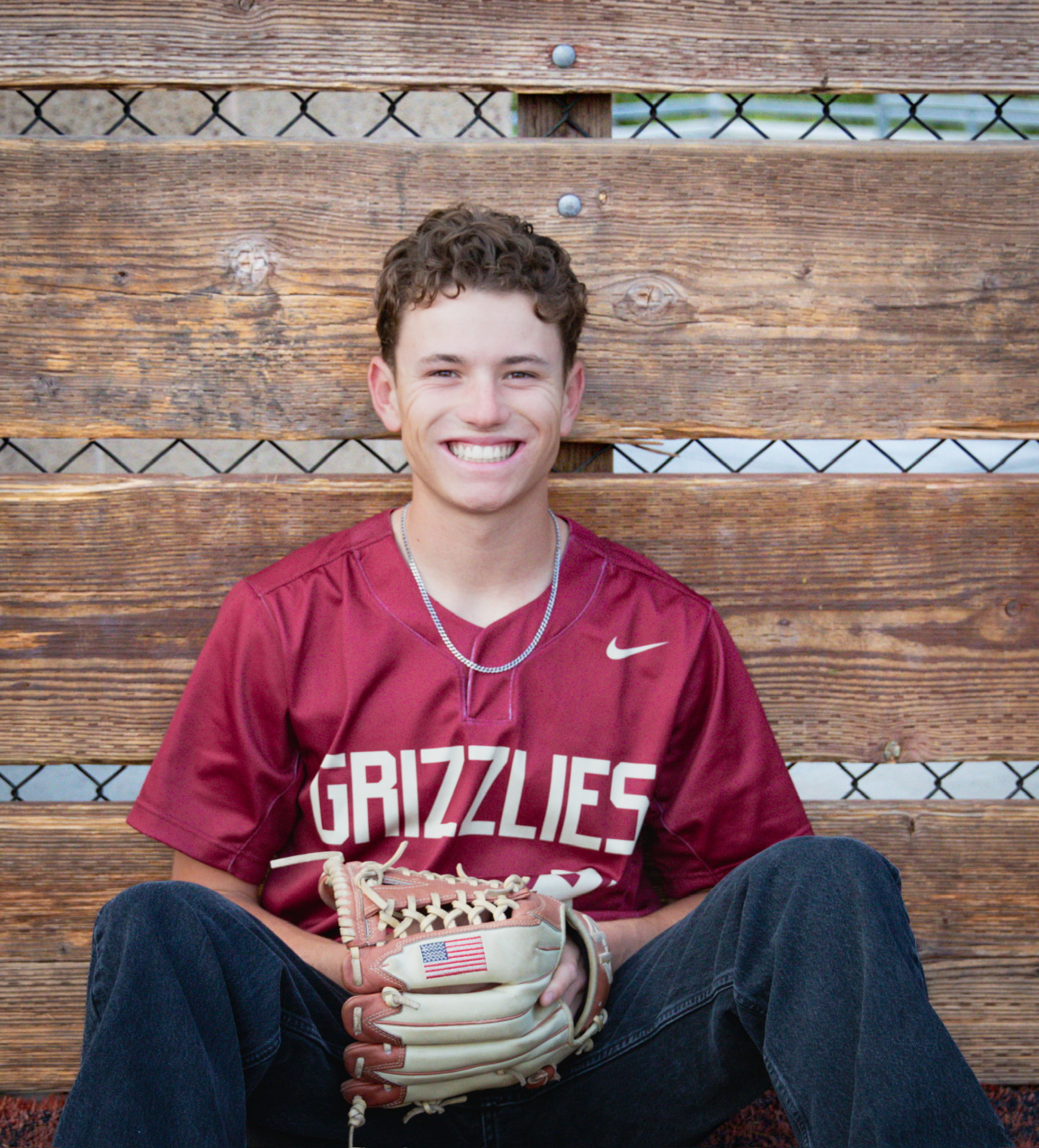 Senior in a maroon Grizzlies baseball jersey sitting on a bench with a glove