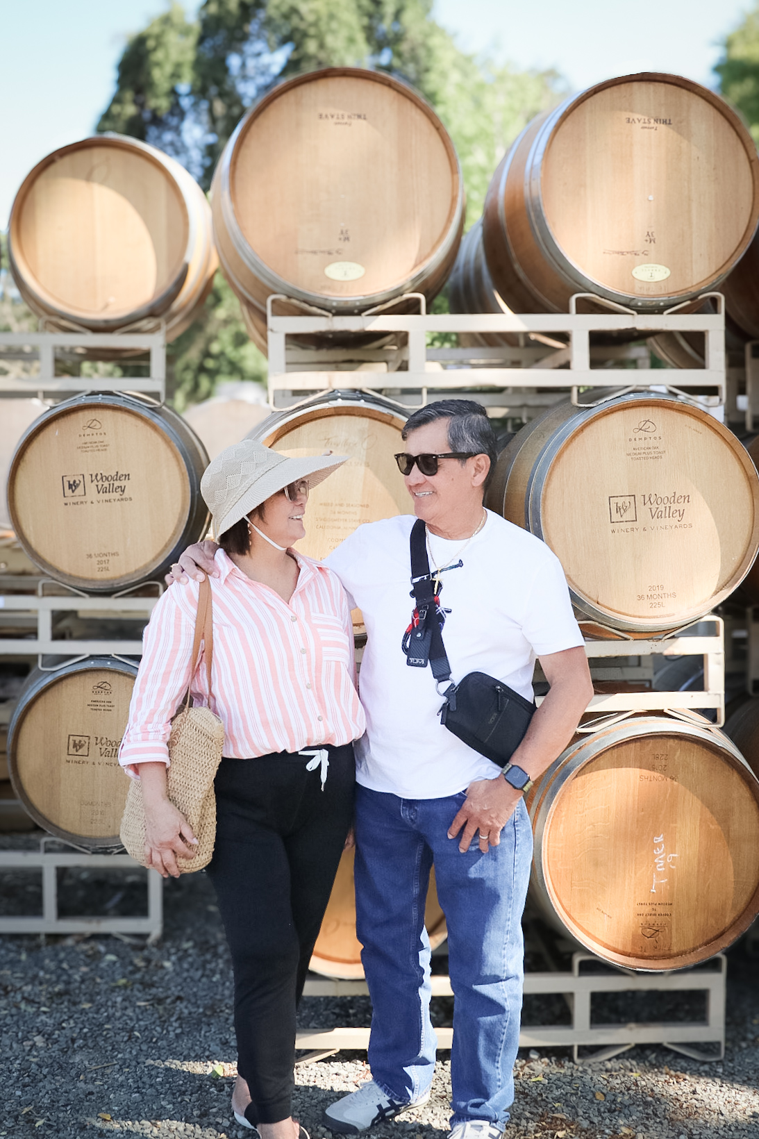 Couple smiling at each other in front of wine barrels at a vineyard