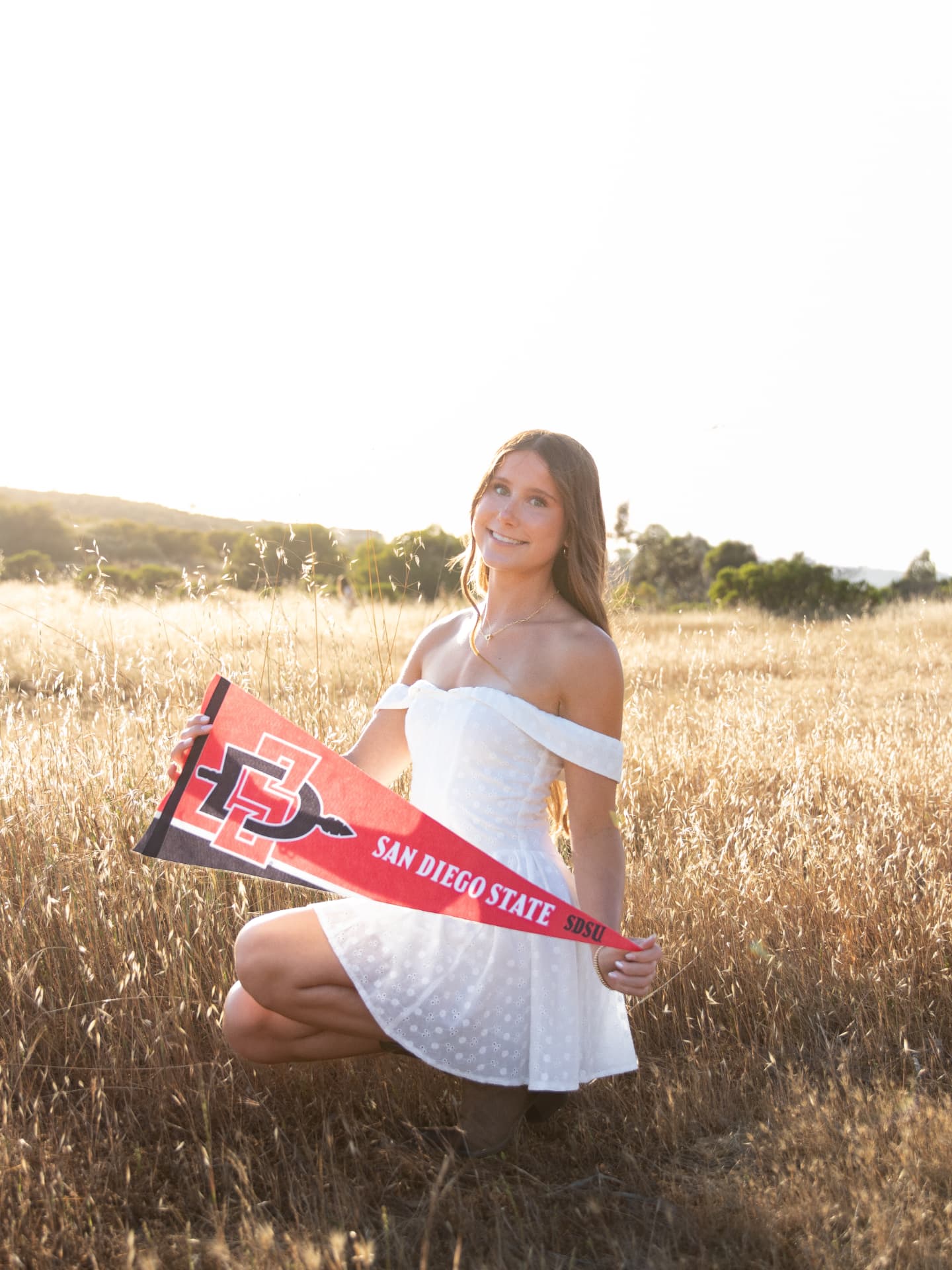 Senior kneeling in a golden field holding a San Diego State pennant