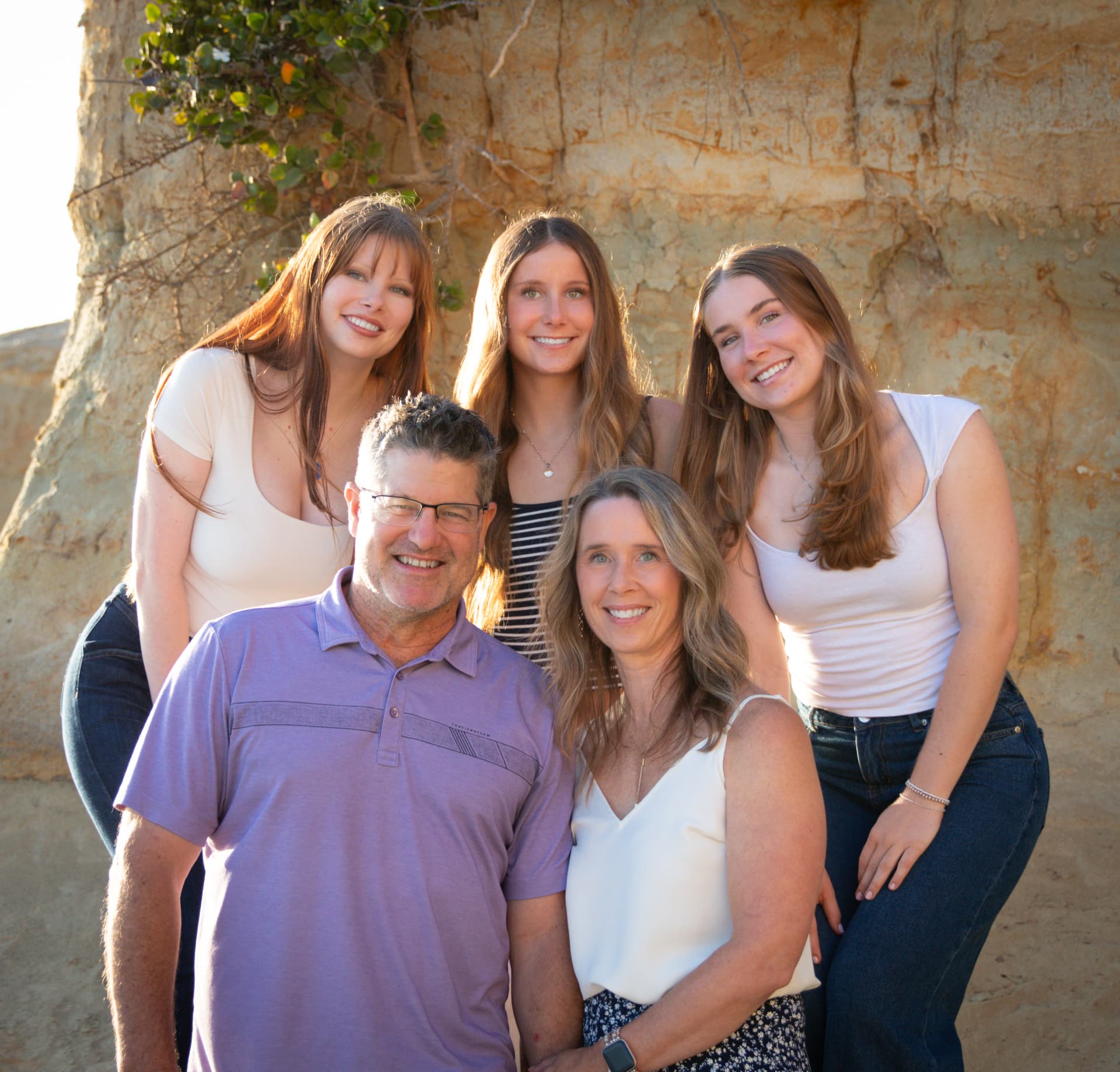 Family of five smiling together against a sandstone bluff at sunset